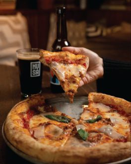 Mão a levantar uma fatia de pizza acabada de sair do forno, com queijo derretido a escorrer/home/klevieco/fontinha.klevie.com