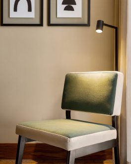 Cadeira estofada a verde junto à janela de um quarto, com dois quadros a preto e branco na parede e a ponta da cama coberta por uma manta mostarda/home/klevieco/fontinha.klevie.com