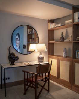 Secretária com espelho redondo por cima, candeeiro de mesa e estante de madeira com peças de decoração, num quarto em tons claros/home/klevieco/fontinha.klevie.com