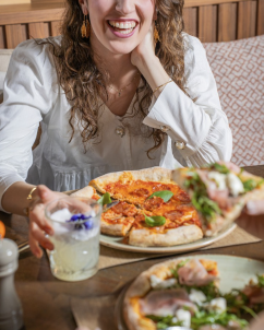 Mulher a sorrir, sentada a uma mesa com um prato de comida à frente/home/klevieco/fontinha.klevie.com