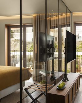 Quarto de hotel com cama de colcha dourada, secretária e porta envidraçada para uma varanda/home/klevieco/fontinha.klevie.com